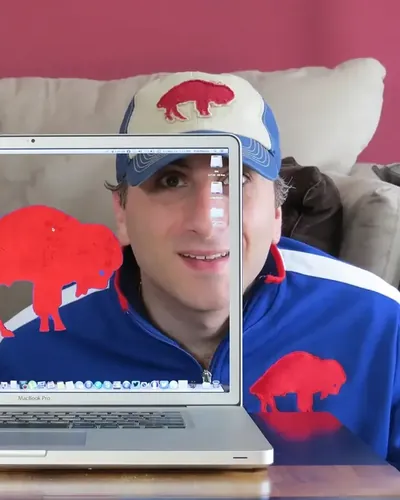 Aldo in a Buffalo Bills cap behind a see-through MacBook Pro